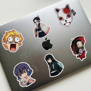May include: A selection of anime character stickers, each with a unique design. The stickers display colourful illustrations of anime figures, including a character with yellow hair and wide eyes, and a character wearing a white mask with red accents.