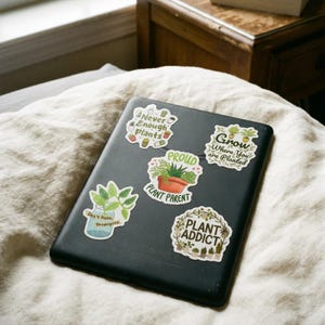 May include: A black tablet featuring five plant-themed stickers. The stickers display the text: Never Enough Plants, Grow Where You are Planted, PROUD PLANT PARENT, Don't Hate, Propagate, and PLANT ADDICT, accompanied by illustrations of various potted plants.