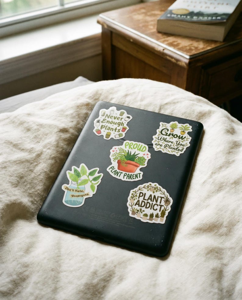 May include: A black tablet featuring five plant-themed stickers. The stickers display the text: Never Enough Plants, Grow Where You are Planted, PROUD PLANT PARENT, Don't Hate, Propagate, and PLANT ADDICT, accompanied by illustrations of various potted plants.