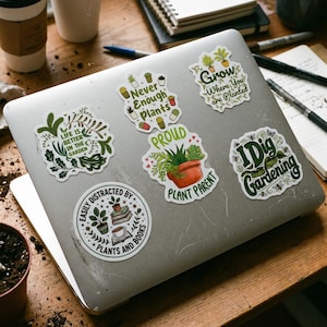 May include: A silver laptop decorated with six vinyl stickers featuring botanical themes and text. The stickers include phrases like 'Life is better in the garden', 'Never enough plants', 'Grow where you are planted', 'Proud plant parent', 'I dig gardening', and 'Easily distracted by plants and books'.