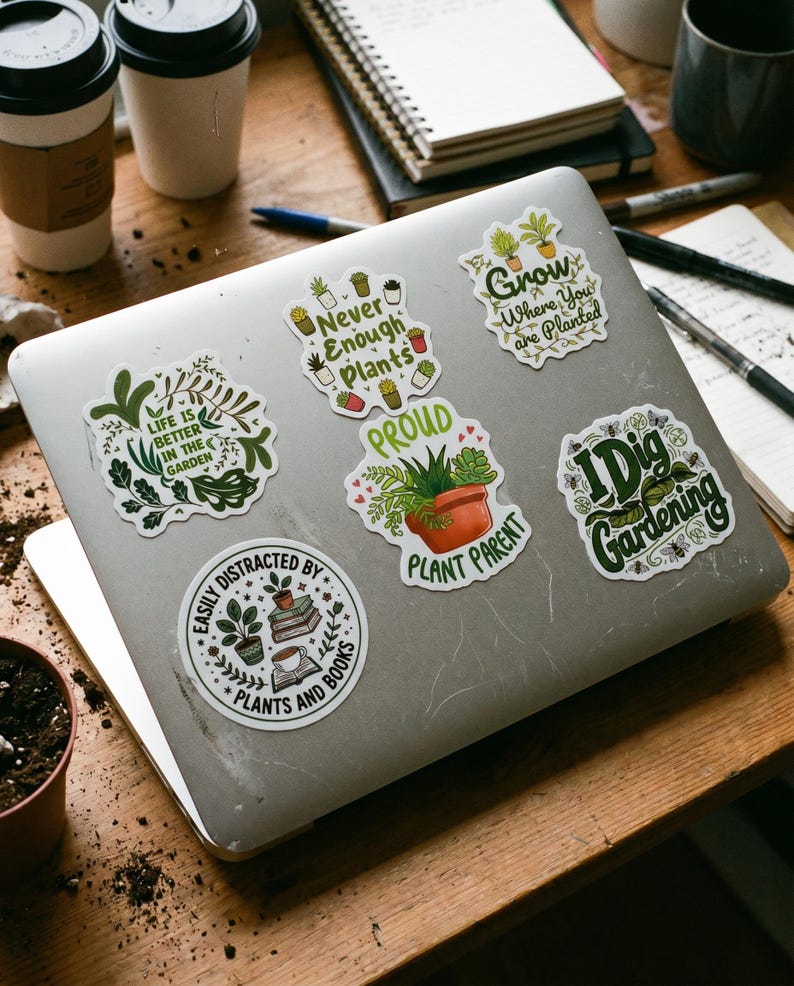May include: A silver laptop decorated with six vinyl stickers featuring botanical themes and text. The stickers include phrases like 'Life is better in the garden', 'Never enough plants', 'Grow where you are planted', 'Proud plant parent', 'I dig gardening', and 'Easily distracted by plants and books'.