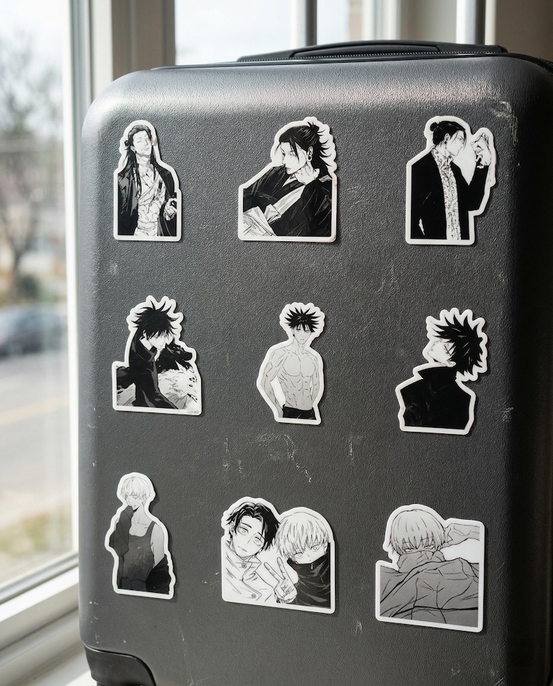 May include: A black suitcase featuring nine individual black and white vinyl stickers. The stickers display various anime-style character illustrations, including portraits, figures in dark clothing, and scenes with multiple characters in a manga art style.