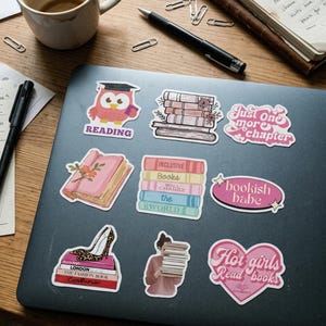 May include: A collection of colorful stickers with book-themed designs on a laptop. The stickers include an owl wearing a graduation cap, stacks of books, and phrases like "Just one more chapter" and "Hot girls Read books."