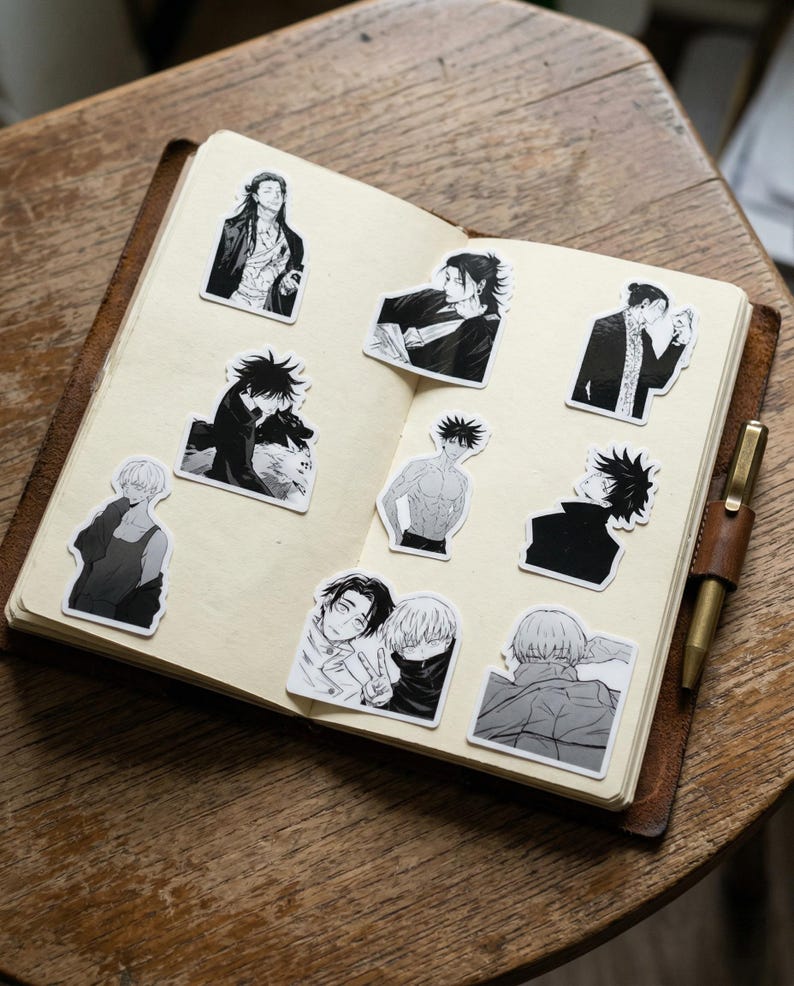 May include: An open notebook with a leather cover containing nine black and white stickers featuring various anime-style character illustrations. The stickers depict different figures in manga art style, including portraits and action poses, arranged on the pages.
