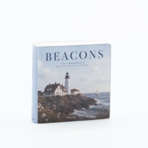 Puede incluir: Un libro en miniatura titulado Beacons: The Lighthouses of the Atlantic Coast. La portada presenta una fotografía de un faro blanco en un acantilado rocoso sobre el océano con un pequeño velero a lo lejos bajo un cielo nublado.