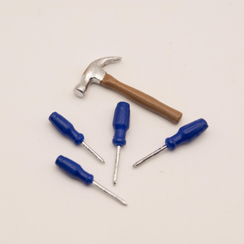 May include: A miniature claw hammer with a silver-toned metal head and a brown handle, accompanied by four small screwdrivers featuring bright blue plastic handles and thin silver-toned metal shafts, arranged together on a plain surface.