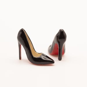 Puede incluir: Dos zapatos de tac&oacute;n negros con suelas rojas. Los zapatos tienen punta afilada y tac&oacute;n de aguja. El interior del zapato es beige. Los zapatos son brillantes y parecen estar hechos de un material duro.
