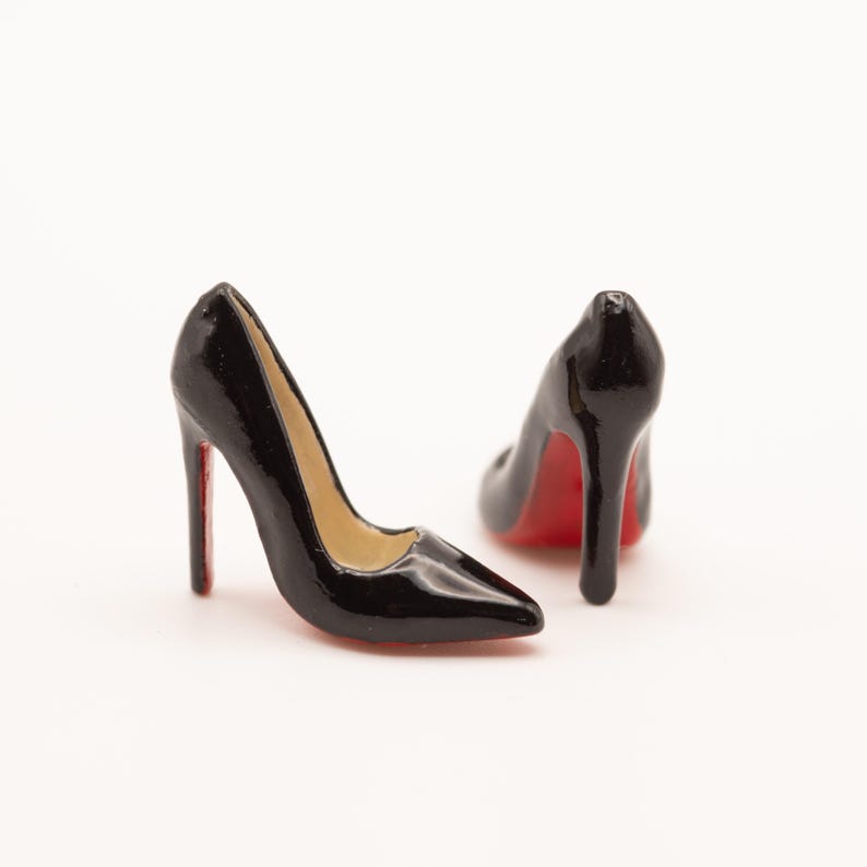 Puede incluir: Dos zapatos de tac&oacute;n negros con suelas rojas. Los zapatos tienen punta afilada y tac&oacute;n de aguja. El interior del zapato es beige. Los zapatos son brillantes y parecen estar hechos de un material duro.