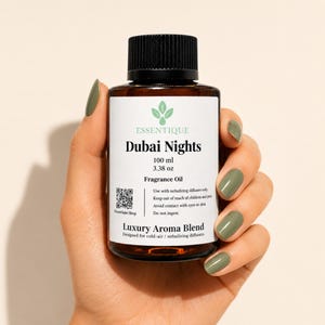 以下が含まれることがあります： 「ドバイナイト」フレグランスオイルの茶色のガラス瓶、100 ml、黒いキャップ付き。ラベルにはブランド名、製品名、使用方法が記載されています。オリーブグリーンのマニキュアを塗った手でボトルを持っています。