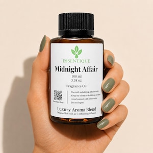 以下が含まれることがあります： 「Midnight Affair」フレグランスオイルの茶色のガラス瓶、100 ml、黒いキャップ付き。ラベルにはブランド名「Essentique」と製品の詳細が含まれています。ボトルは、オリーブグリーンのマニキュアを塗った手で持たれています。