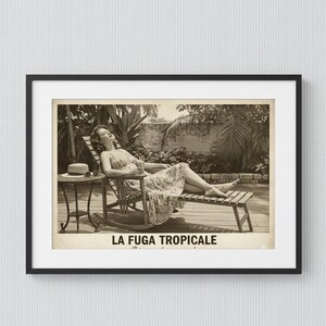May include: Black and white framed print of a woman relaxing on a wooden lounge chair. A small table with a hat and sunglasses sits nearby. The print has the text "LA FUGA TROPICALE" at the bottom.