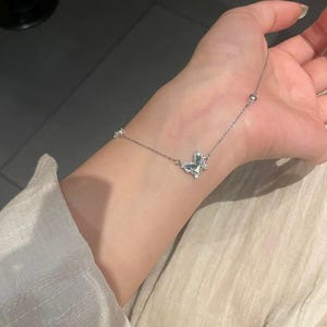 May include: A delicate silver-toned chain bracelet featuring a central butterfly-shaped charm encrusted with small clear stones. The thin metal chain includes evenly spaced small round metallic beads along its length, creating a refined and subtle accessory.