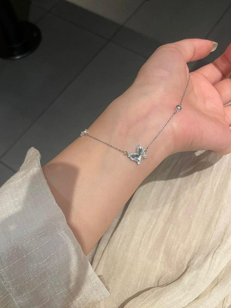 May include: A delicate silver-toned chain bracelet featuring a central butterfly-shaped charm encrusted with small clear stones. The thin metal chain includes evenly spaced small round metallic beads along its length, creating a refined and subtle accessory.