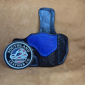 May include: Black leather holster with blue accents and stitching. Features a textured blue panel and a round sticker with the text "Southland Leather Co Benton AR".