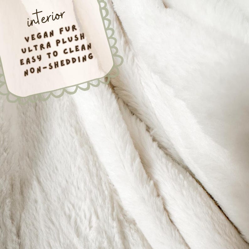 May include: Close-up of a white, plush vegan fur blanket. The blanket has a soft, textured appearance. A tag in the upper left corner reads "interior" and lists features: "VEGAN FUR, ULTRA PLUSH, EASY TO CLEAN, NON-SHEDDING."