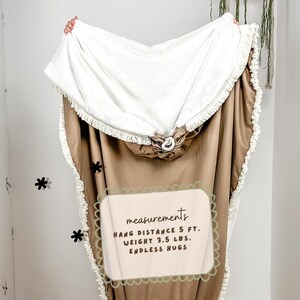 May include: A hooded blanket with a white sherpa lining and a tan exterior. The blanket has a fringed edge and a drawstring closure. The text on the image says "ENDLESS HUGS" and the blanket weighs 3.5 lbs.
