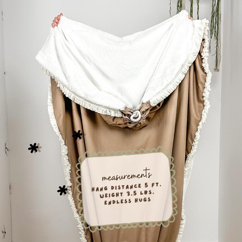 May include: A hooded blanket with a white sherpa lining and a tan exterior. The blanket has a fringed edge and a drawstring closure. The text on the image says "ENDLESS HUGS" and the blanket weighs 3.5 lbs.