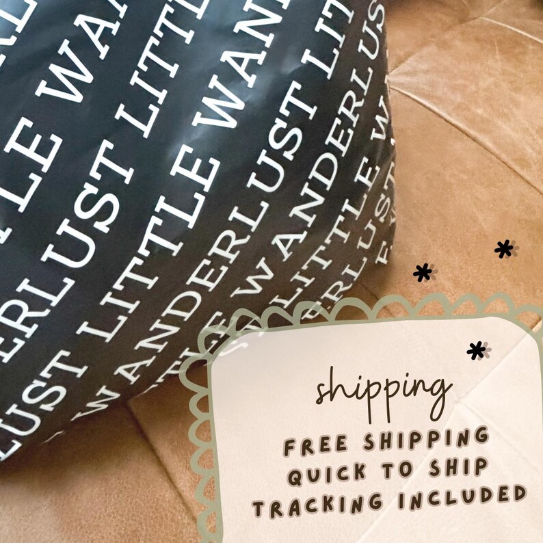 May include: Black wrapping paper with the words "Wanderlust Little" printed in white. The paper is partially rolled up, revealing the text. The background is a brown leather surface.