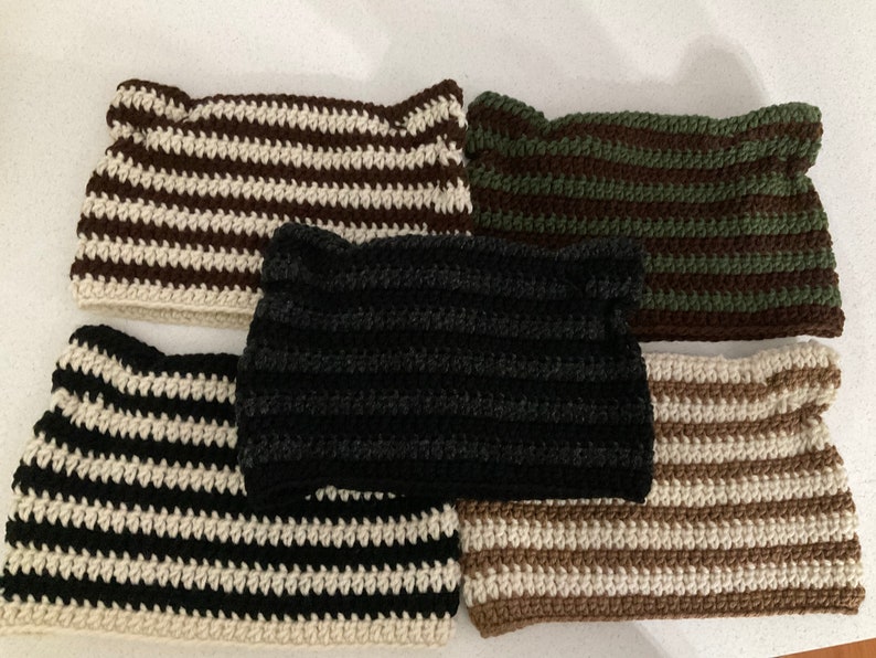 5 striped beanies with cat ears on a light background. From top left, the stripes are beige/brown, forest and brown, black and beige, and coffee and beige. Darker hat in center is black and Heather grey.