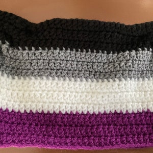 May include: A crocheted scarf with four stripes in black, grey, white, and purple. The scarf is made with a simple stitch pattern.