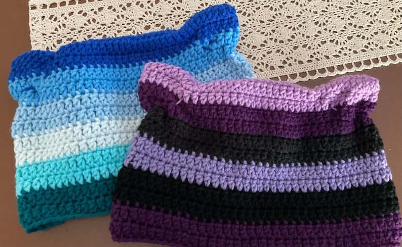 May include: Two crocheted hats with stripes in different color combinations. One hat is blue, teal, and white, and the other is purple, black, and lavender.