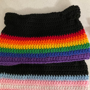 May include: A black crocheted cat ear hat with a rainbow stripe design and a transgender pride flag design. The hat is handmade and features a unique, colourful pattern, perfect for expressing individuality and support.