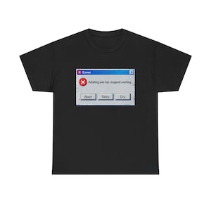 May include: Black t-shirt with a computer error message graphic. The message says "Adulting.exe has stopped working" with options to "Abort", "Retry", or "Cry". The design is styled like a classic Windows error window, offering a humorous take on adulthood.