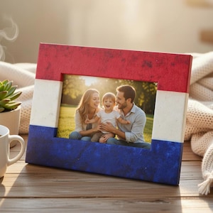 Könnte beinhalten: Ein rechteckiger Bilderrahmen in Rot, Weiß und Blau, der an eine Flagge erinnert. Er enthält ein Familienfoto. Eine Tasse Kaffee und eine kleine Sukkulente im Topf sind im Vordergrund zu sehen.