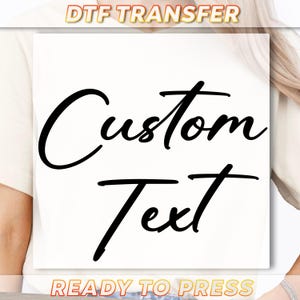 May include: White t-shirt with the words "Custom Text" in a black, cursive font. The words "DTF TRANSFER" and "READY TO PRESS" are in the image.