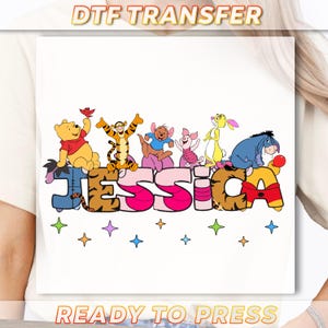 May include: A white DTF transfer featuring the name "Jessica" in a colorful design with characters from a popular animated series. The characters are arranged above the letters, with stars below. The words "DTF TRANSFER" and "READY TO PRESS" are at the top and bottom.