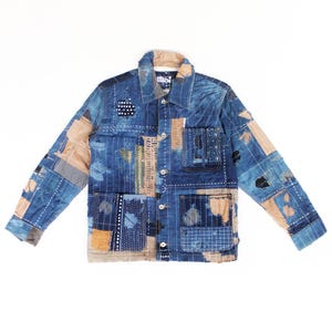 Könnte beinhalten: Blaue Patchwork-Jacke mit Kragen und Knopfverschluss. Die Jacke hat verschiedene Stoffflicken in Blau-, Beige- und Weißtönen mit sichtbaren Nahtdetails. Die Jacke hat zwei Vordertaschen und lange Ärmel.