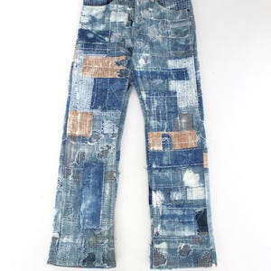 Könnte beinhalten: Blaue Jeans mit Patchwork-Design. Die Jeans haben verschiedene Blautöne, mit Flicken aus beigem und weißem Stoff. Die Jeans haben einen geraden Bein-Schnitt und werden auf weißem Hintergrund präsentiert.