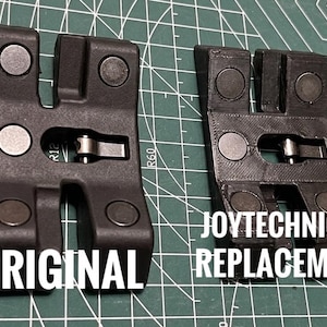 May include: Two black plastic components with silver metal accents and circular magnets. The left component is labeled "ORIGINAL" and the right component is labeled "JOYTECHNICA REPLACEMENT". The components are on a green cutting mat.