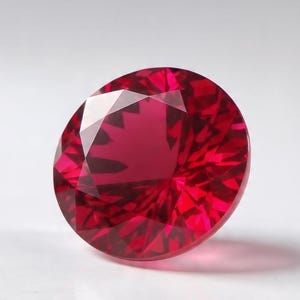 Könnte beinhalten: Ein runder, facettierter Edelstein in einer tiefen, leuchtend roten Farbe. Der Stein weist einen Brillantschliff mit zahlreichen dreieckigen und rautenförmigen Facetten auf, die das Licht reflektieren und ein komplexes Muster erzeugen.