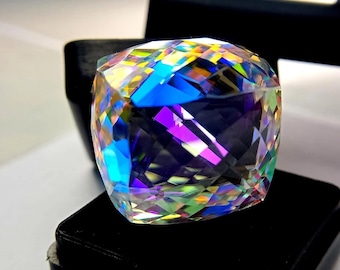 May include: A large, faceted gemstone with a square cushion cut. The gem displays a vibrant array of colors, including blues, purples, greens, and yellows, reflecting light in a dazzling display. The gem is set against a black background.