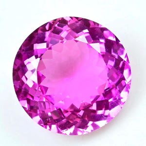 Könnte beinhalten: Ein runder, facettierter Edelstein in Rosa- und Magentatönen. Der Edelstein hat einen Brillantschliff, der das Licht reflektiert und einen funkelnden Effekt erzeugt. Der Edelstein ist vor einem weißen Hintergrund platziert.