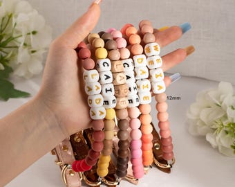 May include: A collection of personalized dog collars with names spelled out in white letter beads. The collars are in various colors, including pink, brown, and orange. The adjustable buckle can be extended by 2 inches, and the beads are 12mm.
