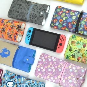 May include: A collection of colorful zippered cases with various patterns, including video game characters and symbols, surrounding a Nintendo Switch console. The cases feature designs in orange, blue, green, and purple, with a variety of button and zipper closures.