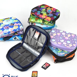 May include: A collection of colorful zippered game card cases, some open to display card slots. The cases feature various patterns, including cartoon characters and abstract designs. Two game cards are visible. The Blue Robotto logo is in the bottom left corner.