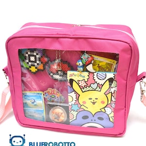Puede incluir: Bolso de hombro rosa con una ventana frontal transparente que muestra varios artículos con temática Pokémon. Incluye una tarjeta de Pikachu, una tarjeta de Piplup y un diseño de cuentas. El bolso tiene una correa rosa y cierre de cremallera.