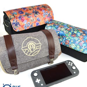 May include: Three gaming console carrying cases with colorful character designs, alongside a gray handheld console. One case is gray with brown straps and a gold emblem. The other two cases have black bases and patterned tops.
