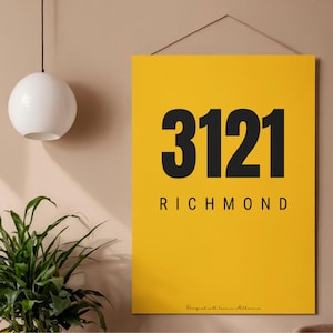 May include: A yellow rectangular wall art print with the numbers "3121" in bold black font, and the word "RICHMOND" below. The print is hanging on a wall. The bottom right corner of the print has the text "Designed with love in Melbourne."