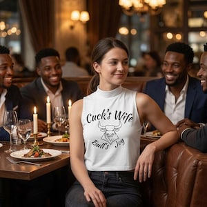 May include: A white sleeveless mock neck crop top featuring a black graphic of a bull head and the text "Cuck's Wife Bull's Joy" printed on the front. The garment is paired with dark denim jeans, showcasing a casual and fitted design.