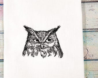 May include: White kitchen towel featuring a detailed black embroidered owl design. The owl's face is centered, showcasing intricate feather details and piercing eyes. The towel is folded, with the owl's image prominently displayed.