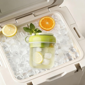 May include: A refreshing drink in a clear glass with a green lid, lemon slices, and ice cubes, inside a white cooler. The cooler also contains ice, a lemon half, an orange slice, and mint leaves.
