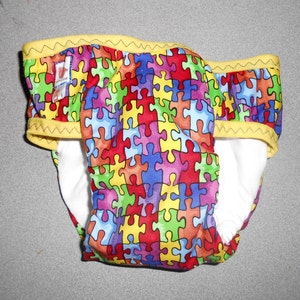 May include: A colourful reusable cloth nappy with a yellow zig-zag trim and a jigsaw puzzle pattern.