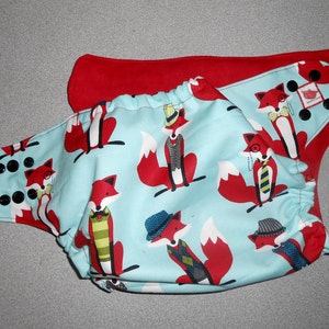 May include: A blue and red cloth diaper with a pattern of foxes wearing hats and ties. The diaper has snaps and elastic around the legs.