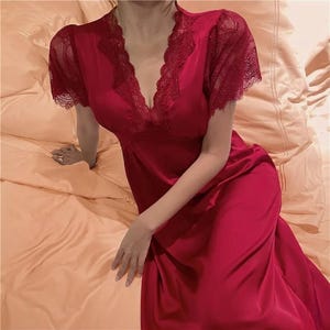May include: A red satin nightgown with lace trim around the neckline and short sleeves. The V-neckline is accentuated with delicate lace, and the dress has a flowing, floor-length design. The fabric has a subtle sheen, suggesting a luxurious feel.