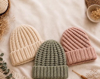 Puede incluir: Tres gorros de punto en colores crema, verde salvia y rosa empolvado. Cada gorro presenta un borde acanalado grueso y doblado, con un patrón de punto vertical texturizado en toda la corona. Los gorros están dispuestos uno junto al otro.