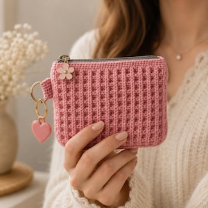 Puede incluir: Un monedero rectangular de ganchillo en color rosa empolvado con textura de punto de gofre. El tirador de la cremallera est&aacute; adornado con un peque&ntilde;o dije de flor de esmalte rosa claro y una anilla dorada con un colgante de coraz&oacute;n rosa.